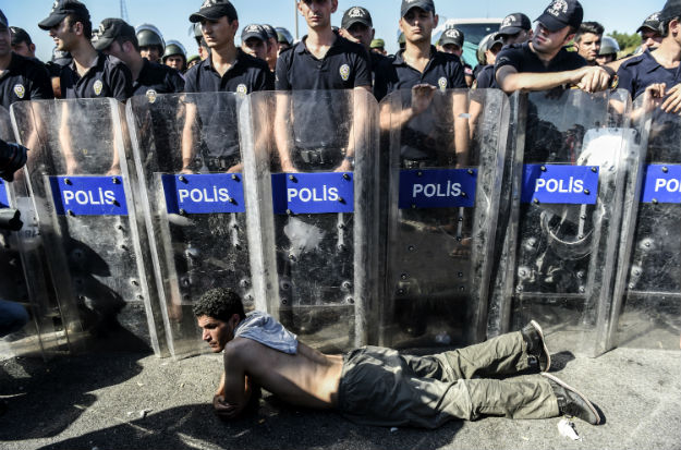 Syryjski uchodźca leży przed szpalerem tureckich policjantów